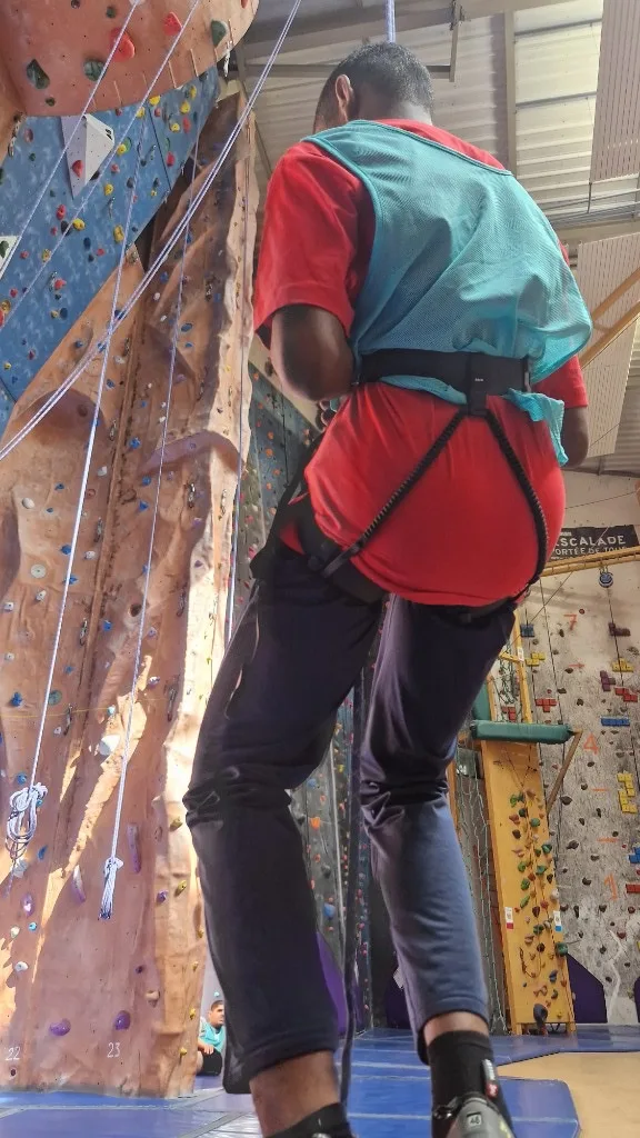 Jeune équipé d'un baudrier en séance d'escalade en salle avec ARK