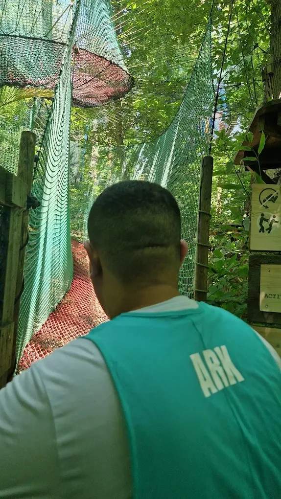 Jeune en tenue ARK sur un parcours d'accrobranche dans les arbres, filets de sécurité autour