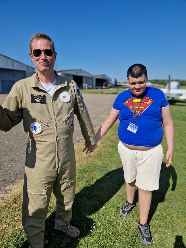 Un jeune accompagné main dans la main par un pilote lors d'une sortie découverte à l'aérodrome