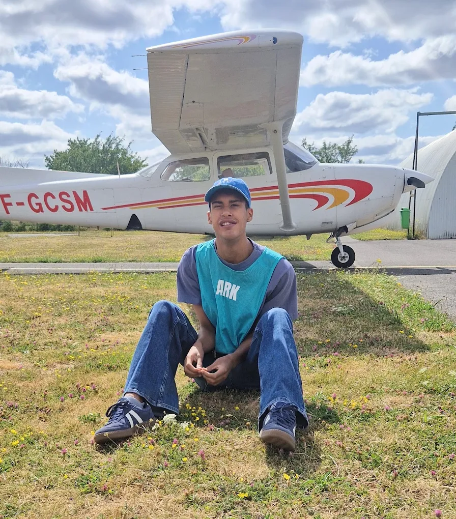 Jeune souriant assis devant un avion lors d'une sortie découverte à l'aérodrome
